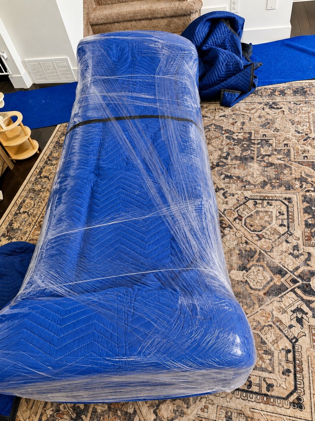 Household furniture covered with blue moving blankets and plastic wrap